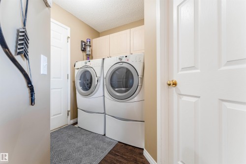 Laundry area featuring side-by-side washer and dryer, upper cabinetry, and wood-finish flooring - 847 Blacklock Way, Edmonton, AB - Indoor Photo Showing Laundry Room