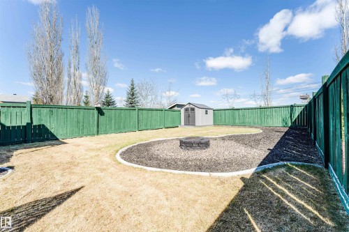 Spacious backyard featuring a green privacy fence, a detached storage shed, a defined bark mulch area with a built-in fire pit, and an expansive lawn - 847 Blacklock Way, Edmonton, AB - Outdoor