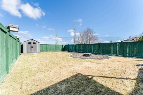 Expansive fenced backyard featuring a storage shed, a fire pit area with dark mulch, and a green privacy fence - 847 Blacklock Way, Edmonton, AB - Outdoor