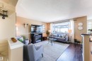 Living area featuring dark wood-finish flooring, a large window with white curtain panels, and a built-in electric fireplace unit - 847 Blacklock Way, Edmonton, AB  - Indoor Photo Showing Living Room 