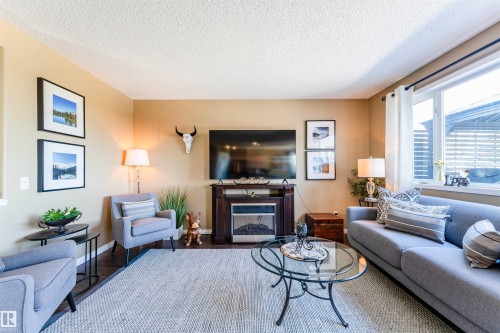 Living area featuring a floor-to-ceiling window, dark wood-finish flooring, and a built-in fireplace with a dark wood surround - 847 Blacklock Way, Edmonton, AB - Indoor Photo Showing Living Room With Fireplace