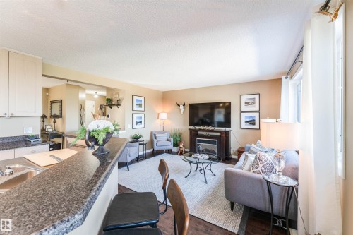 Open-concept living space featuring wood-finish flooring, a built-in electric fireplace, a breakfast bar with stone-look countertops, and recessed lighting - 847 Blacklock Way, Edmonton, AB - Indoor Photo Showing Living Room