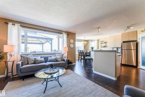 Open-concept living area featuring dark wood-finish flooring, a large window, a kitchen island with seating, stainless steel appliances, and track lighting - 847 Blacklock Way, Edmonton, AB - Indoor Photo Showing Living Room