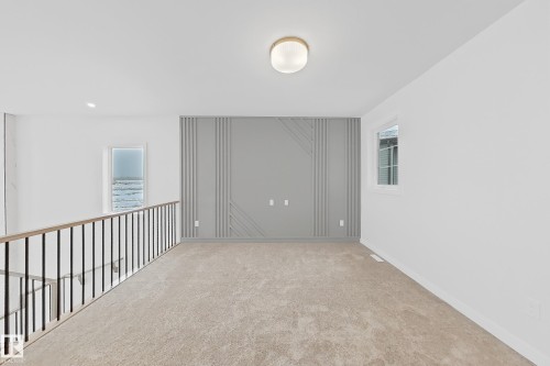 The property features a bright open space with carpeted flooring, a decorative accent wall, a modern ceiling light fixture, and two windows providing natural light - 17 Trill Point(E), Spruce Grove, AB - Indoor Photo Showing Other Room