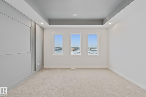 This room features light-colored carpeting, three windows, and a tray ceiling with recessed lighting - 17 Trill Point(E), Spruce Grove, AB - Indoor Photo Showing Other Room