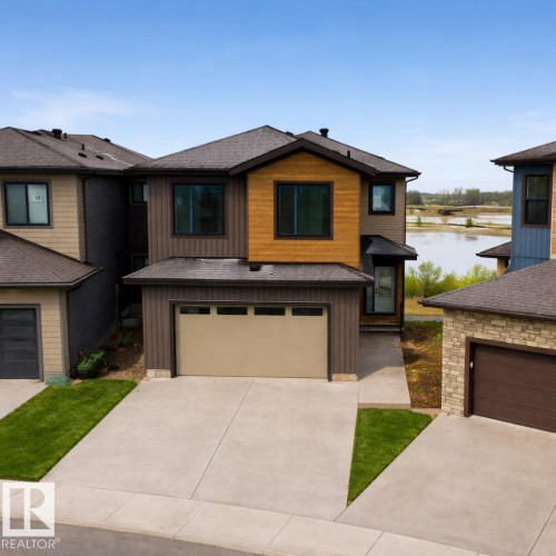 The property features a two-story exterior with a blend of brown and wood-toned siding, a dark roof, and an attached garage with a light-colored door - 17 Trill Point(E), Spruce Grove, AB - Outdoor