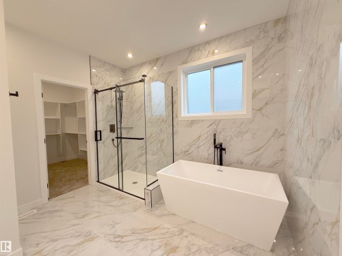 Bathroom featuring marble-look tiled walls and flooring, a freestanding bathtub with a matte black fixture, a glass-enclosed shower with a matte black frame, and a window - 17 Trill Point(E), Spruce Grove, AB - Indoor Photo Showing Bathroom