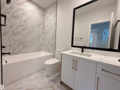 Bathroom featuring a white bathtub, a toilet, a vanity with a white countertop and gold hardware, and a large mirror - 17 Trill Point(E), Spruce Grove, AB - Indoor Photo Showing Bathroom