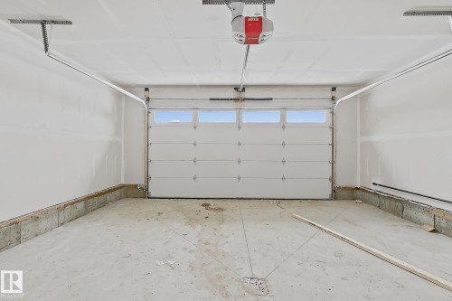 The property includes a spacious garage with a white overhead door featuring upper window panels, and a ceiling-mounted garage door opener - 17 Trill Point(E), Spruce Grove, AB - Indoor Photo Showing Garage
