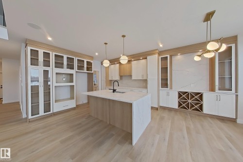The property features a bright kitchen with light-toned flooring, a central island with a waterfall countertop, and modern pendant lighting - 17 Trill Point(E), Spruce Grove, AB - Indoor Photo Showing Kitchen