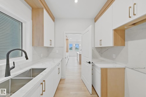 The kitchen features white cabinetry with gold-toned hardware, quartz countertops, a dual basin sink with a black faucet, and light wood flooring - 17 Trill Point(E), Spruce Grove, AB - Indoor Photo Showing Kitchen