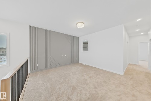 This bright interior space features neutral-toned carpeting, a contemporary accent wall with geometric paneling, and a modern ceiling light fixture - 17 Trill Point(E), Spruce Grove, AB - Indoor Photo Showing Other Room