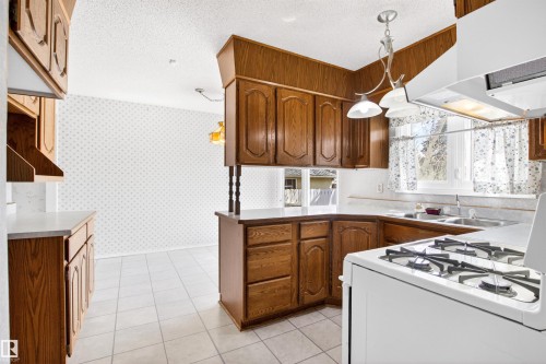 Kitchen featuring wood-finish cabinetry, white tiled flooring, and a white gas range with overhead ventilation - 29 Bristow Crescent, Spruce Grove, AB - Indoor Photo Showing Kitchen