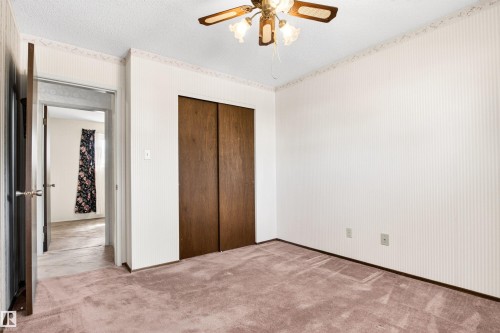 Carpeted room featuring a ceiling fan with light fixture, white patterned wallpaper, and a dark wood bifold closet door - 29 Bristow Crescent, Spruce Grove, AB - Indoor Photo Showing Other Room