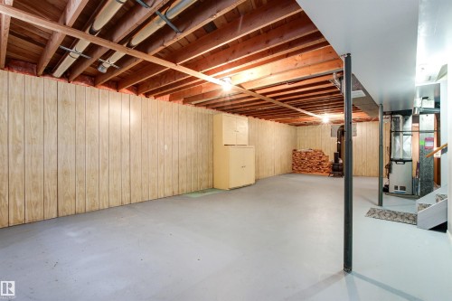 Spacious unfinished basement featuring exposed wood joists, light wood-finish paneling, painted concrete flooring, and built-in storage cabinets - 29 Bristow Crescent, Spruce Grove, AB - Indoor Photo Showing Basement