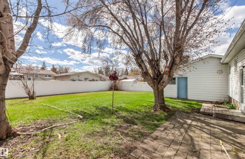 Expansive backyard featuring a lush lawn, established trees, a white perimeter fence, and a paver patio - 29 Bristow Crescent, Spruce Grove, AB - Outdoor