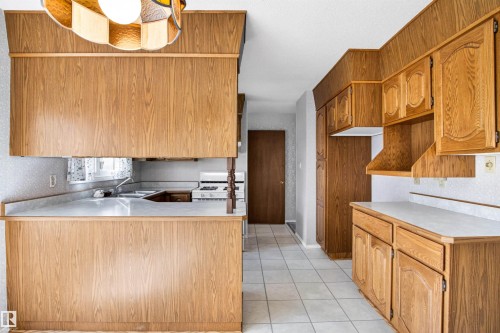 Kitchen featuring wood-finish cabinetry, white countertops, a built-in range, a double basin sink, and tile flooring - 29 Bristow Crescent, Spruce Grove, AB - Indoor Photo Showing Kitchen