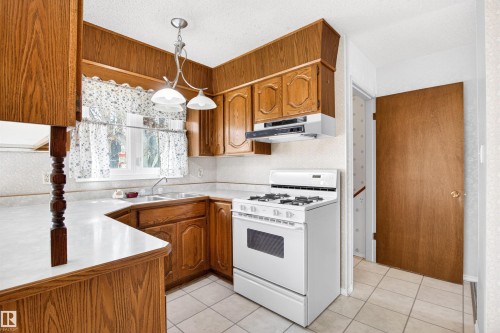 Kitchen featuring wood-finish cabinetry, white countertops, tile flooring, a double basin sink, and a white gas range - 29 Bristow Crescent, Spruce Grove, AB - Indoor Photo Showing Kitchen With Double Sink