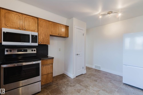 Kitchen featuring warm-toned wood cabinetry, black countertops, and a black tile backsplash - 3752 114 Street, Edmonton, AB - Indoor Photo Showing Kitchen