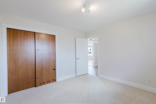Light-colored carpeting and white walls in a room featuring wood-finish sliding closet doors, white baseboards, and a track lighting fixture - 3752 114 Street, Edmonton, AB - Indoor Photo Showing Other Room