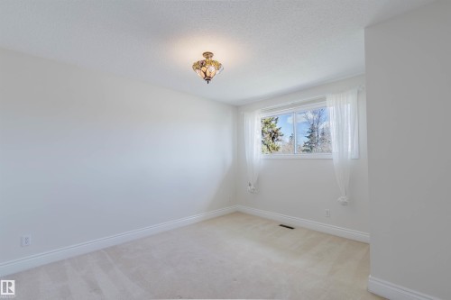 Light-filled room featuring a single window with white trim, a decorative ceiling light fixture, neutral carpeting, and white baseboards - 3752 114 Street, Edmonton, AB - Indoor Photo Showing Other Room