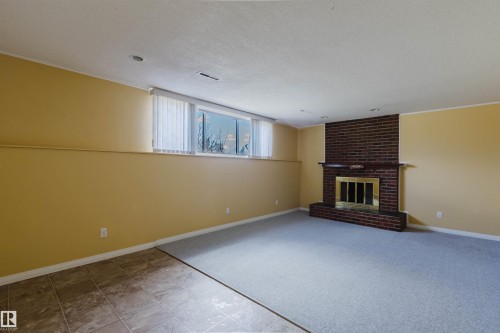 Spacious room featuring a brick fireplace with a gold-toned insert and mantel, light-toned carpeting, and a tiled entry area - 3752 114 Street, Edmonton, AB - Indoor With Fireplace