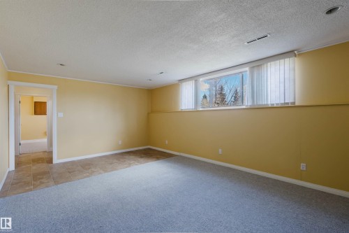 Spacious room featuring a large window with vertical blinds, recessed lighting, neutral-toned walls, and a combination of gray carpet and tiled flooring - 3752 114 Street, Edmonton, AB - Indoor Photo Showing Other Room