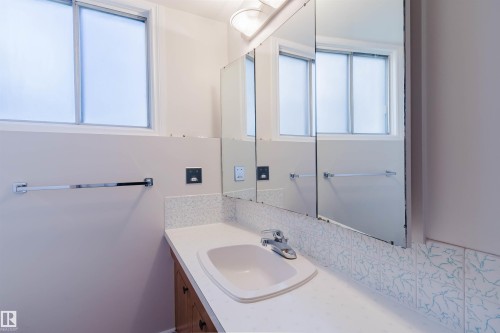 Bathroom vanity featuring a built-in sink with chrome faucet, a white countertop, and a wood-finish cabinet - 3752 114 Street, Edmonton, AB - Indoor Photo Showing Bathroom