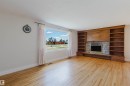 Expansive living space featuring wood-finish flooring, a stone-surround fireplace with a brass firebox, and built-in wood shelving - 3752 114 Street, Edmonton, AB  - Indoor Photo Showing Living Room With Fireplace 