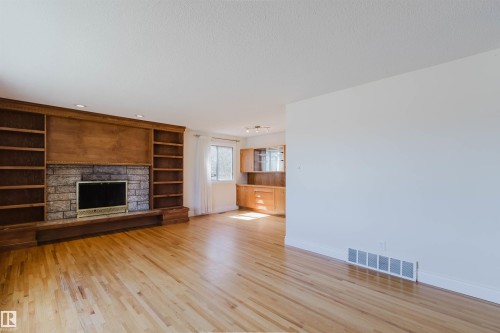 Spacious living area featuring wood-finish flooring, a stone-faced fireplace, and extensive built-in wooden shelving - 3752 114 Street, Edmonton, AB - Indoor Photo Showing Living Room With Fireplace
