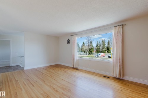 Spacious room featuring light wood-finish flooring, a large picture window, white baseboards, and a neutral wall color - 3752 114 Street, Edmonton, AB - Indoor Photo Showing Other Room