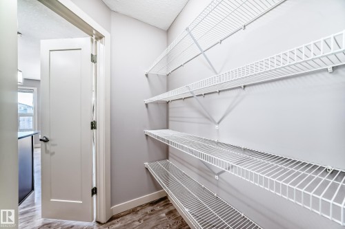 Spacious pantry featuring multiple tiers of white wire shelving, light grey wall finish, and wood-finish flooring - 1669 Hammond Crescent Nw, Edmonton, AB - Indoor With Storage