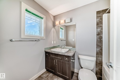 Bathroom featuring a wood-finish vanity with a surface-mounted sink, a large wall mirror, and a toilet - 1669 Hammond Crescent Nw, Edmonton, AB - Indoor Photo Showing Bathroom