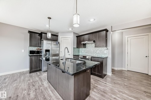 Kitchen featuring a large island with dark countertop and undermount sink, pendant lighting, wood-finish flooring, dark cabinetry, and stainless steel appliances - 1669 Hammond Crescent Nw, Edmonton, AB - Indoor Photo Showing Kitchen With Double Sink With Upgraded Kitchen