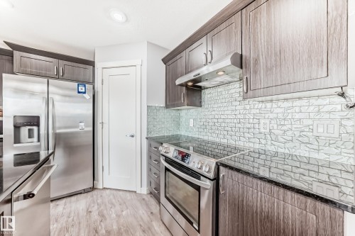 Kitchen featuring wood-finish cabinetry, stainless steel appliances, dark countertops, a textured tile backsplash, and recessed lighting - 1669 Hammond Crescent Nw, Edmonton, AB - Indoor Photo Showing Kitchen With Upgraded Kitchen