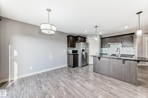Open-concept living space featuring wood-finish flooring, a kitchen island with a dark countertop, stainless steel appliances, dark wood cabinetry, and a patterned backsplash - 1669 Hammond Crescent Nw, Edmonton, AB - Indoor Photo Showing Kitchen With Upgraded Kitchen