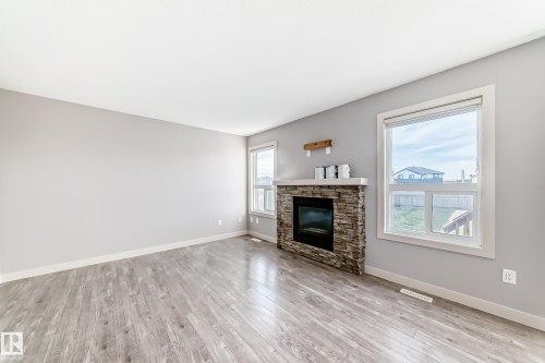 Living area featuring a stone-clad fireplace with a hearth, light-toned wood-finish flooring, and two large windows with white trim - 1669 Hammond Crescent Nw, Edmonton, AB - Indoor Photo Showing Living Room With Fireplace
