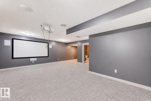 Spacious entertainment area featuring a mounted projector, large projection screen, built-in ceiling speakers, recessed lighting, and plush carpeting - 1669 Hammond Crescent Nw, Edmonton, AB - Indoor Photo Showing Other Room