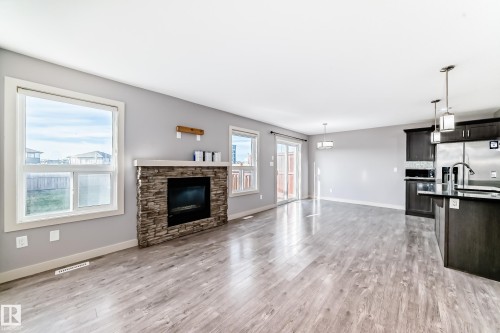 Open-concept living space featuring wood-finish flooring, a stacked stone fireplace with a white mantel, and multiple large windows - 1669 Hammond Crescent Nw, Edmonton, AB - Indoor With Fireplace