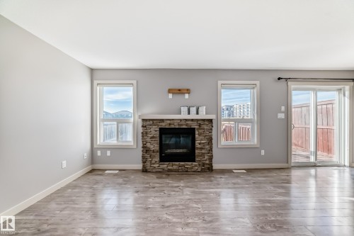 Living area featuring a stone-clad fireplace with a light-colored mantel, wood-finish flooring, and recessed lighting - 1669 Hammond Crescent Nw, Edmonton, AB - Indoor Photo Showing Living Room With Fireplace
