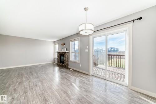 Spacious interior featuring wide plank wood-finish flooring, a stone-clad fireplace, and multiple windows - 1669 Hammond Crescent Nw, Edmonton, AB - Indoor With Fireplace