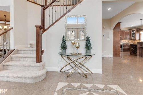 The property features a grand staircase with carpeted steps and a polished wood handrail, an arched doorway, and polished tile flooring with an inlaid design - 6002 46 Avenue, Beaumont, AB - Indoor Photo Showing Other Room
