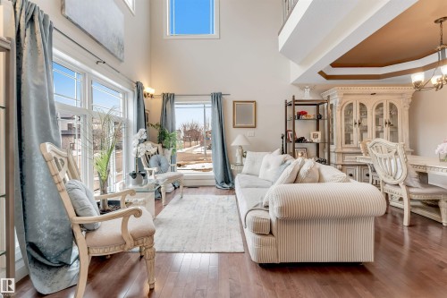 This living area features rich hardwood flooring, high ceilings, and expansive windows that provide abundant natural light - 6002 46 Avenue, Beaumont, AB - Indoor Photo Showing Living Room