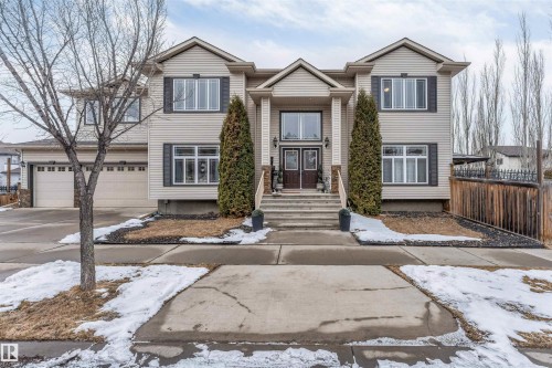 The property features a two-story exterior with light-colored siding, dark window shutters, and a prominent front entrance with double doors and decorative columns - 6002 46 Avenue, Beaumont, AB - Outdoor With Facade