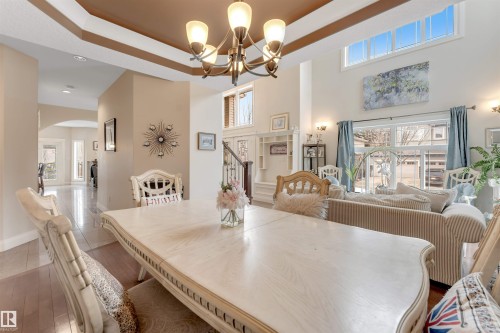 This spacious interior features a tray ceiling with a chandelier, hardwood floors, and a bright living area with tall windows providing abundant natural light - 6002 46 Avenue, Beaumont, AB - Indoor Photo Showing Dining Room