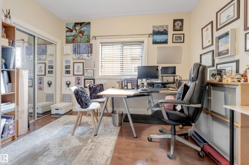 The room features hardwood flooring, a window with horizontal blinds, and a built-in closet with mirrored sliding doors - 6002 46 Avenue, Beaumont, AB - Indoor Photo Showing Office