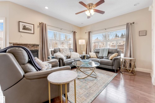 The living room features hardwood flooring, a stone-faced fireplace, and large windows that provide abundant natural light - 6002 46 Avenue, Beaumont, AB - Indoor Photo Showing Living Room With Fireplace