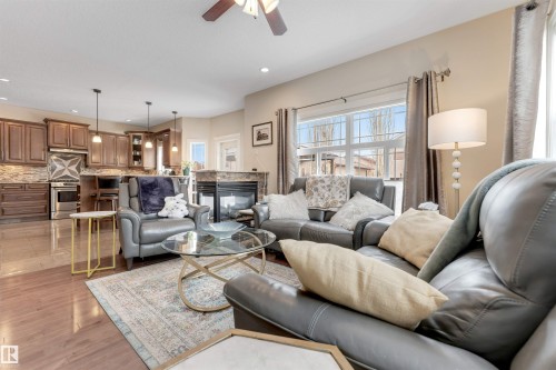 The open concept living area features hardwood flooring, a fireplace with a stone surround, and windows providing natural light - 6002 46 Avenue, Beaumont, AB - Indoor Photo Showing Living Room