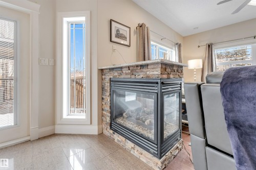 Living area featuring a corner gas fireplace with stone surround, large windows providing natural light, and tile flooring - 6002 46 Avenue, Beaumont, AB - Indoor With Fireplace
