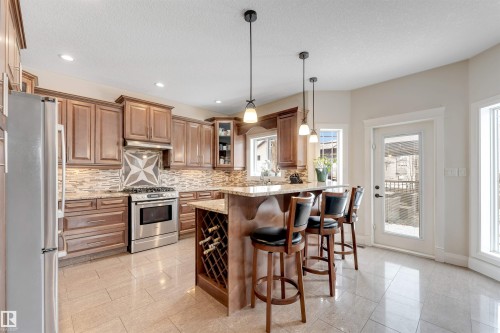 The kitchen features extensive wooden cabinetry, stainless steel appliances, a center island with bar seating, and tile flooring - 6002 46 Avenue, Beaumont, AB - Indoor Photo Showing Kitchen With Upgraded Kitchen